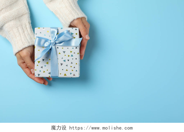 蓝色背景上手拿礼物盒子持有浅蓝色背景礼品盒的年轻女子